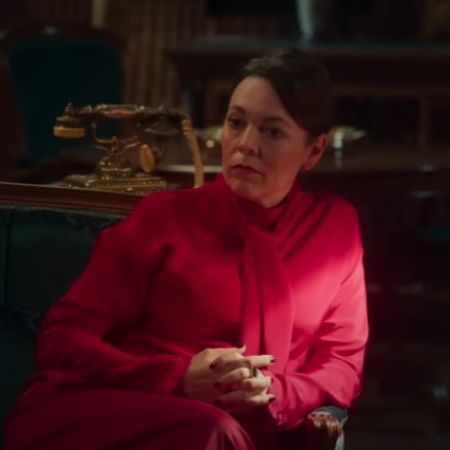 Olivia Colman is on her pink dress sitting with her legs crossed.